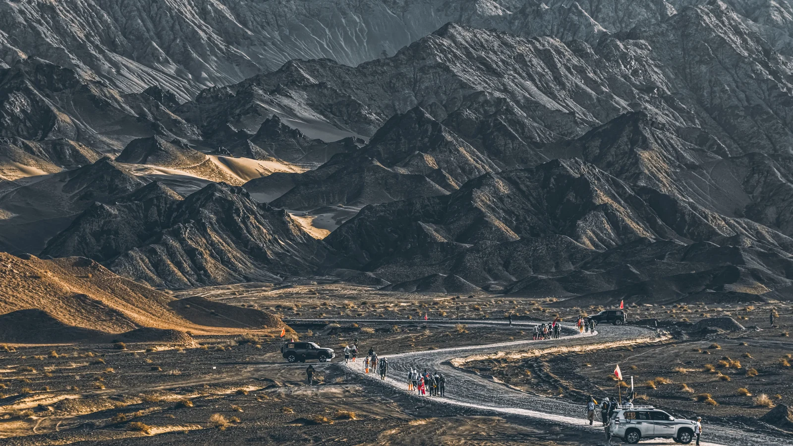 晨光下的荒野山地,一队参与者沿下方道路行进